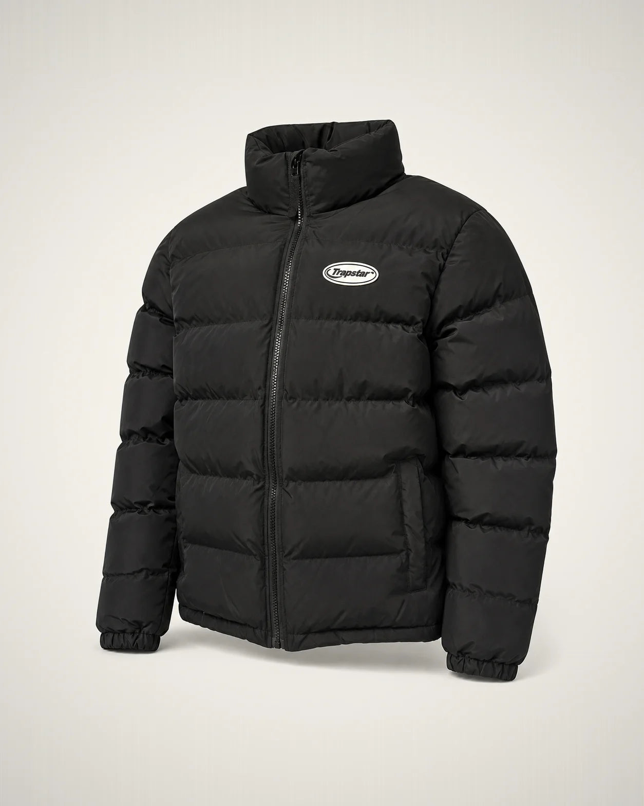 Puffer negra de cuello alto con badge ovalado blanco y cámaras acolchadas anchas.